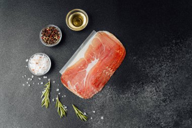 Siyah arka planda tuz, biber ve bitkilerle dilimlenmiş jambon paketi.