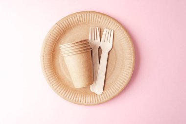 Çevre dostu kavram için pembe arka plan fincanları ve ahşap çatallı Kraft kağıt sofra takımı