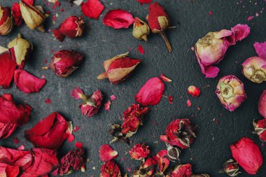 Kurumuş gül tomurcukları ve yapraklar koyu dokulu arka planda, canlı kırmızı ve pembe renkler, doğal botanik elementler