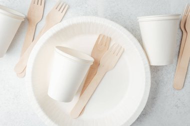 Beyaz tek kullanımlık tabaklara dağılmış beyaz kağıt bardaklar ve ahşap çatallar.