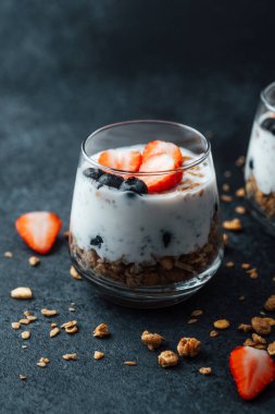 Yoğurtlu granola parfe, koyu arkaplanda çilek ve yabanmersini.