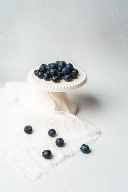 Küçük bir kaide, hafif bir kumaş zemin üzerinde taze yaban mersini taşır..