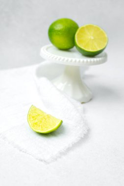 Parlak yeşil limonlar, yanında limon dilimi olan dekoratif bir kaide üzerinde dururlar..