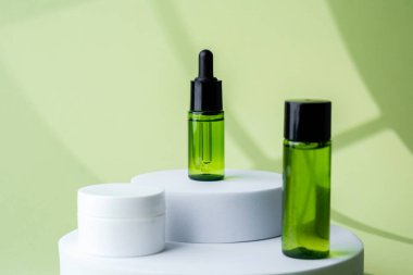Dairesel kaide üzerine sergilenen yeşil kozmetik şişesi ve beyaz krema kavanozları