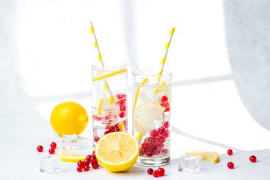 İki uzun bardakta limon kırmızısı üzümlü su ve sarı çizgili kamışlı beyaz masa!