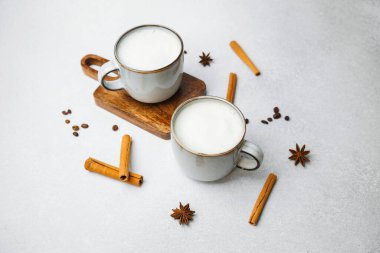 İki sıcak kupa kremalı latte ve tarçınlı çubuklarla desenli bir yüzeye..