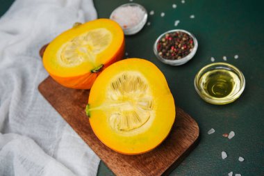 Yarısı turuncu balkabağı kesme tahtasında yağ ve baharatla, koyu yeşil arka plan, kapat