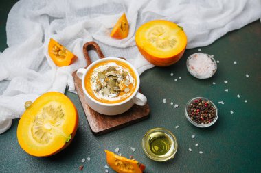 Tahtaya tohum ve krema konmuş sıcak balkabağı çorbası. Etrafı taze balkabağı parçaları ve baharatlarla çevrili..