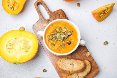 Tohumlarla kaplı taze kabak çorbası ahşap bir tahtanın üzerinde, dilimlenmiş balkabağı kabağıyla servis edilen kabuklu ekmek..