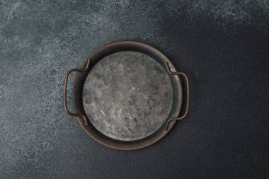 Koyu, desenli bir yüzey üzerinde duran sapları olan yuvarlak metal bir tepsi..