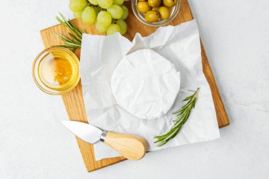 Peynir tabağında yumuşak peynir, bal, yeşil üzüm ve tahta üzerinde zeytin sergilenir..