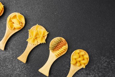 Farklı makarna şekilleri ahşap kaşıklarda canlı renkler ve dokular gösterir..