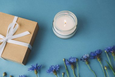 Mavi arka planda çiçek olan hediye kutusu ve mum.