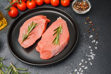 Siyah seramik tabakta çiğ biftek, biberiye, kiraz, domates, tuz ve biber.