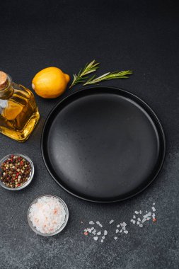 Yemek hazırlamak için limon, otlar ve çeşitli baharatlarla çevrili siyah bir tabak..
