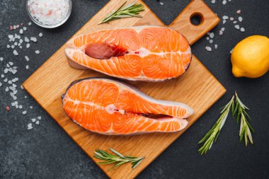 İki canlı somon filetosu limon ve otlarla dolu bir kesim tahtasının üzerinde sergileniyor..