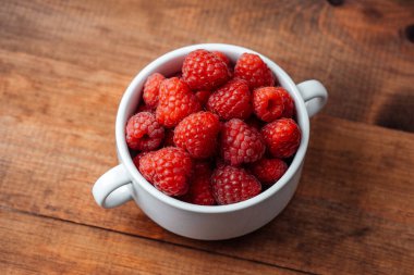 Beyaz kasede ahududu. Kırsal gıda tasarımı ya da organik yeme konsepti için ahşap masa üzerinde