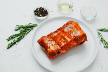 Beyaz tabakta marine edilmiş domuz pirzolası, biberiye ve baharatlı.