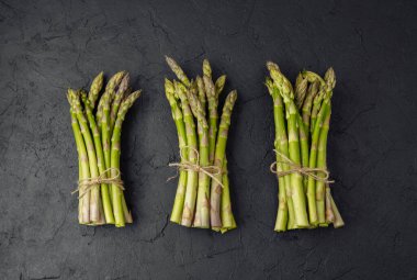 Siyah arka planda sicimle bağlanmış üç demet yeşil kuşkonmaz