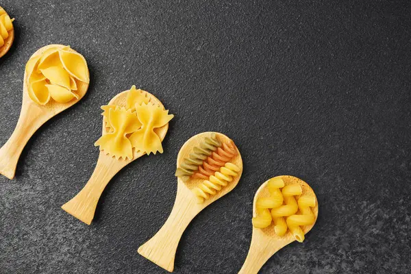 Farklı makarna şekilleri ahşap kaşıklarda canlı renkler ve dokular gösterir..