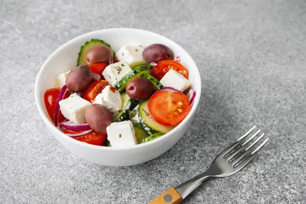 Yunan salatası, beyaz salatalık, salatalık, domates, soğan, çatal ve açık gri arka plan.