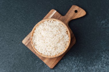 Beyaz basmati pilavı ahşap kase içinde kesme tahtasının üzerinde koyu arkaplanda