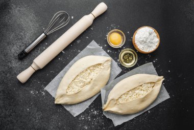 Malzemelerin üst görüntüsü ve iki pişmemiş khachapuri un kaplı siyah masa üzerinde