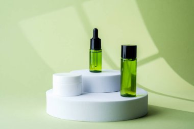 Dairesel kaide üzerine sergilenen yeşil kozmetik şişesi ve beyaz krema kavanozları