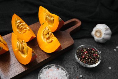 Tahtada çekirdekli turuncu balkabağı parçaları, sarımsak, karabiber ve tuz, koyu arkaplan