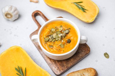 Bir kase kremalı balkabağı çorbası kabak tohumlarıyla süslenmiş, kızarmış ekmek ve taze biberiye ile servis edilmiş.