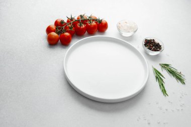 Beyaz arka planda tuz, biber, domates ve biberiye ile boş beyaz tabak
