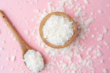 Ahşap kase ve kaşık, pastel pembe arka planda soya yağı taneleri.