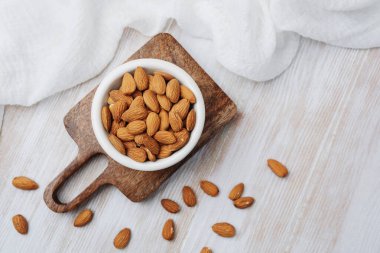 Tahta üzerinde organik badem kasesi ve ışık yüzeyine saçılmış fındıklar.