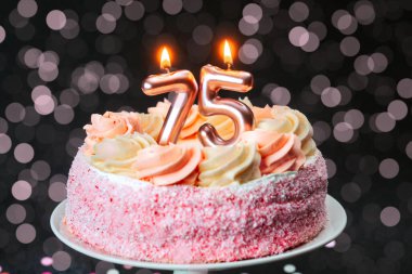 Mumlarla süslenmiş pembe bir pasta, şenlik ortamında 75. yaş gününü kutluyor..