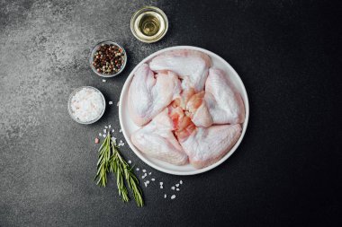 Baharatlı baharatlı tavuk kanatları ve koyu taşlı arka planda yağ.