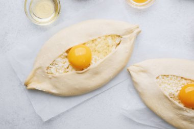Beyaz mutfak yüzeyinde yumurta ve un ile iki khachapuri ekmeğinin üst görüntüsü