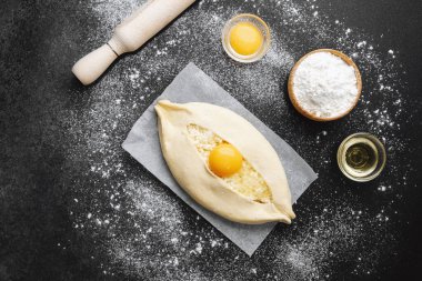 Çiğ khachapuri, yumurta sarısı ve parşömen üzerinde peynir ve siyah arka planda un.