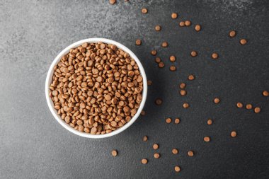 Siyah arka planda kuru köpek mamasıyla dolu beyaz kase ve dağınık mamalar.