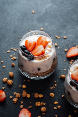 Yoğurtlu granola parfe, koyu arkaplanda çilek ve yabanmersini.