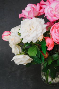 Pembe ve beyaz güller açık cam vazoda koyu arkaplanda