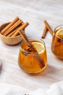 İki bardak baharatlı kehribar içeceği, tarçın çubukları, limon dilimleri ve beyaz ahşap bir masada yıldız anason..