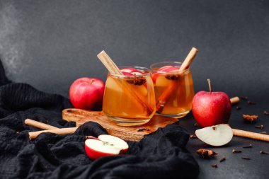 Arkaplanda tarçın çubukları ve elmalar olan ılık elma şarabı.