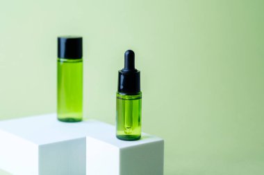 Siyah kapaklı yeşil kozmetik atık şişesi beyaz küp kaide arka planında eşleşen konteynır sergileniyor