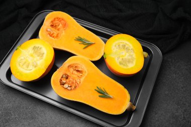 Koyu bir yemek tepsisinde biberiye filizleriyle taze tereyağlı kabak yarımları pişmeye hazır.