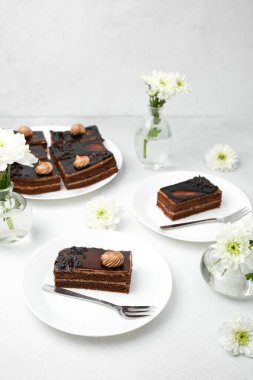 Beyaz tabaklarda beyaz çiçekler ve çatallarla servis edilen zengin çikolatalı pasta dilimleri.