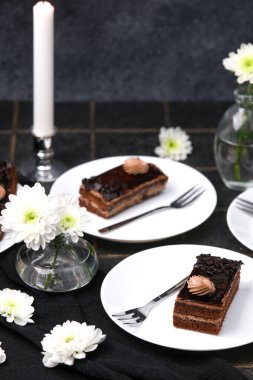 Kremalı ve çiçekli çikolatalı kekler mumun yanındaki karanlık masada.