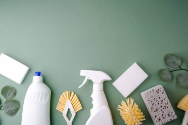 Soluk yeşil bir yüzeyde temizlik malzemeleri şişeleri fırçalar süngerler ve yeşil yapraklar