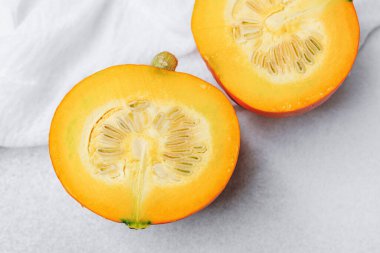 Turuncu balkabağı, beyaz kumaşlı açık gri bir yüzeyde tohumları göstererek ikiye bölünmüş.