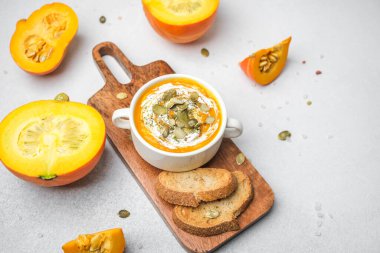 Bir kase krema ve çekirdekli balkabağı çorbası. Tahta bir tahtanın üzerinde kesilmiş balkabaklarıyla servis ediliyor.