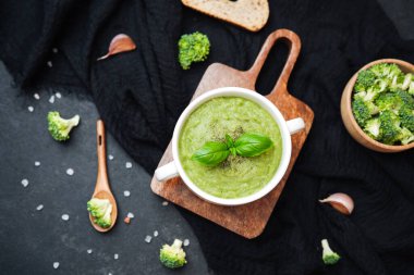 Fesleğen ve biberle süslenmiş beyaz bir kâsede kremalı brokoli çorbası, ekmekle servis edilir.